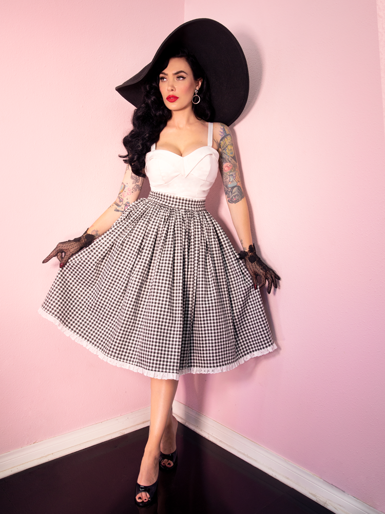 Wearing black lace gloves with a white and black gingham print skirt, Micheline Pitt sports the Maneater Top in White from Vixen Clothing which offers a wide array of retro inspired clothing pieces and accessories.