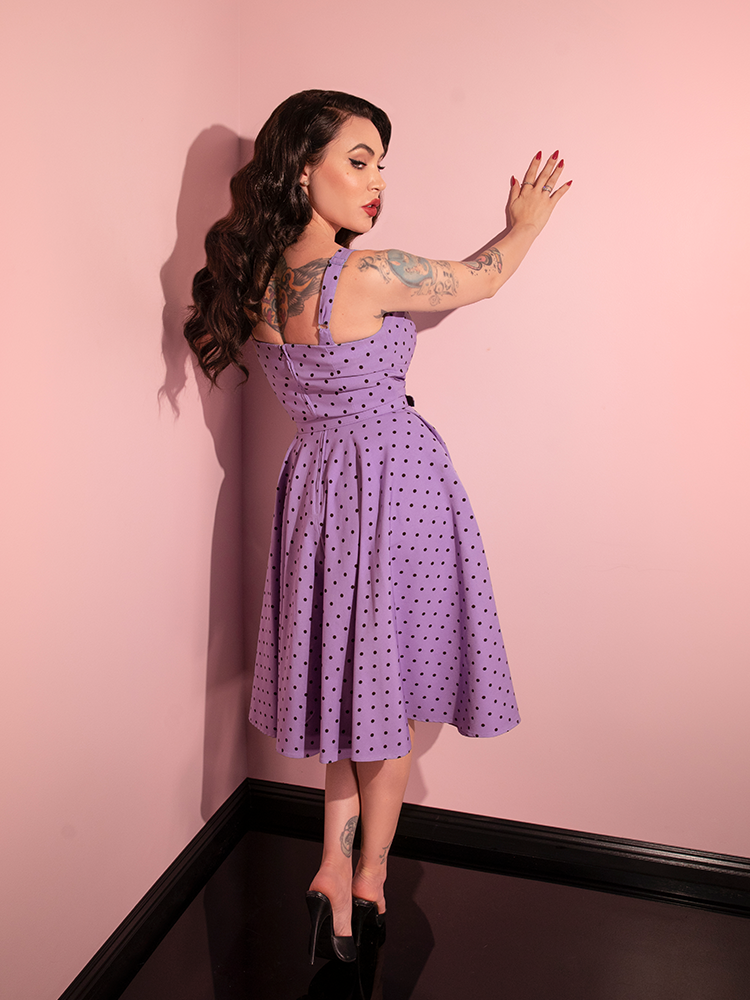 Micheline Pitt infuses her poses with a playful elegance while wearing the Sunset Purple Polka Dot Maneater Swing Dress from the iconic retro dress brand Vixen Clothing.