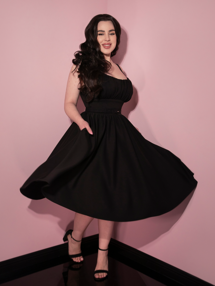 Rachel Sedory smiling and twirling in the Cozy Ingenue Dress in Black paired with black heeled shoes.