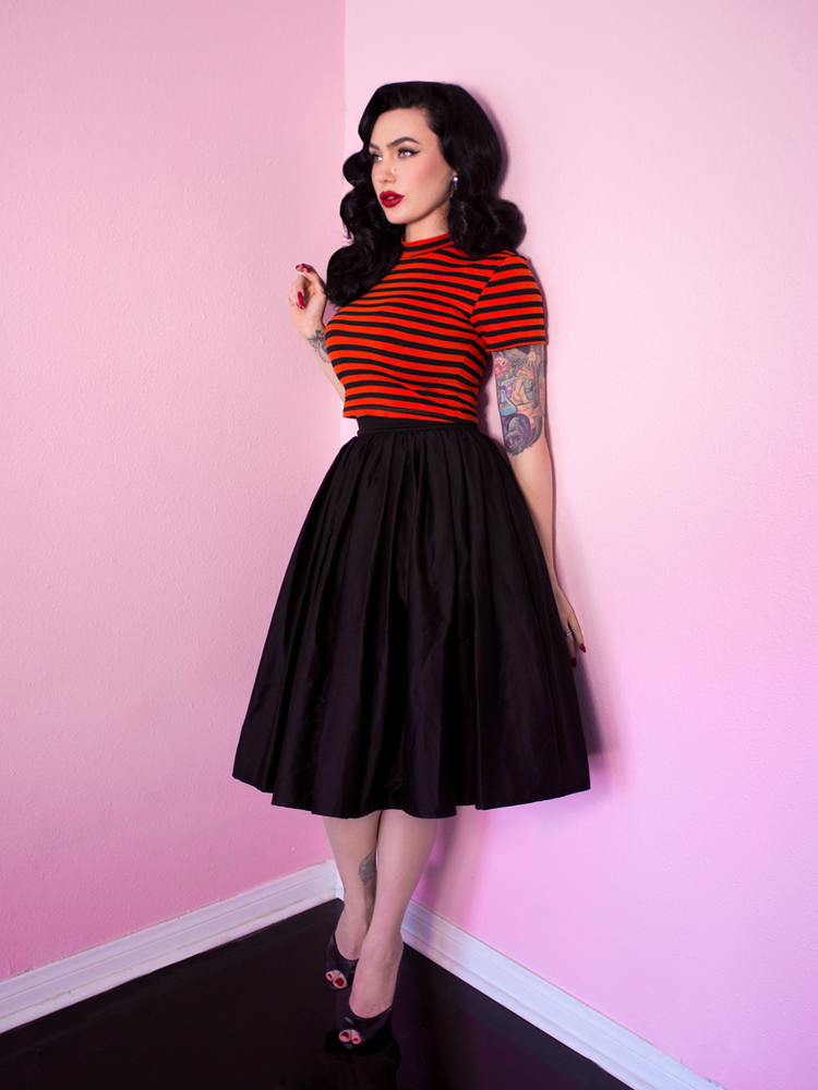A full shot of Micheline Pitt modeling the Bad Girl crop top in orange and black stripes from Vixen Clothing.